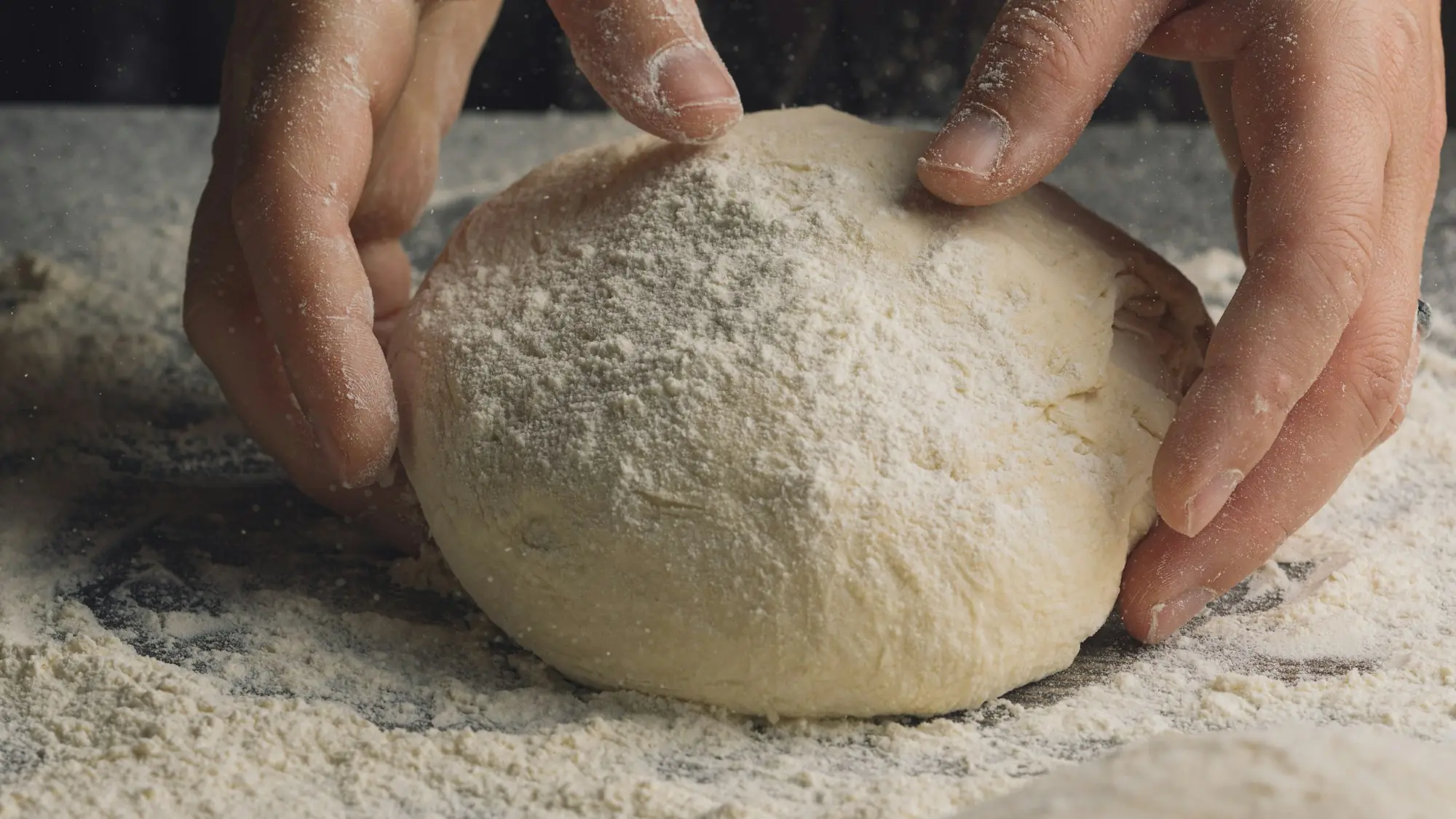 Manos dando forma a una bola de masa sobre una mesa enharinada